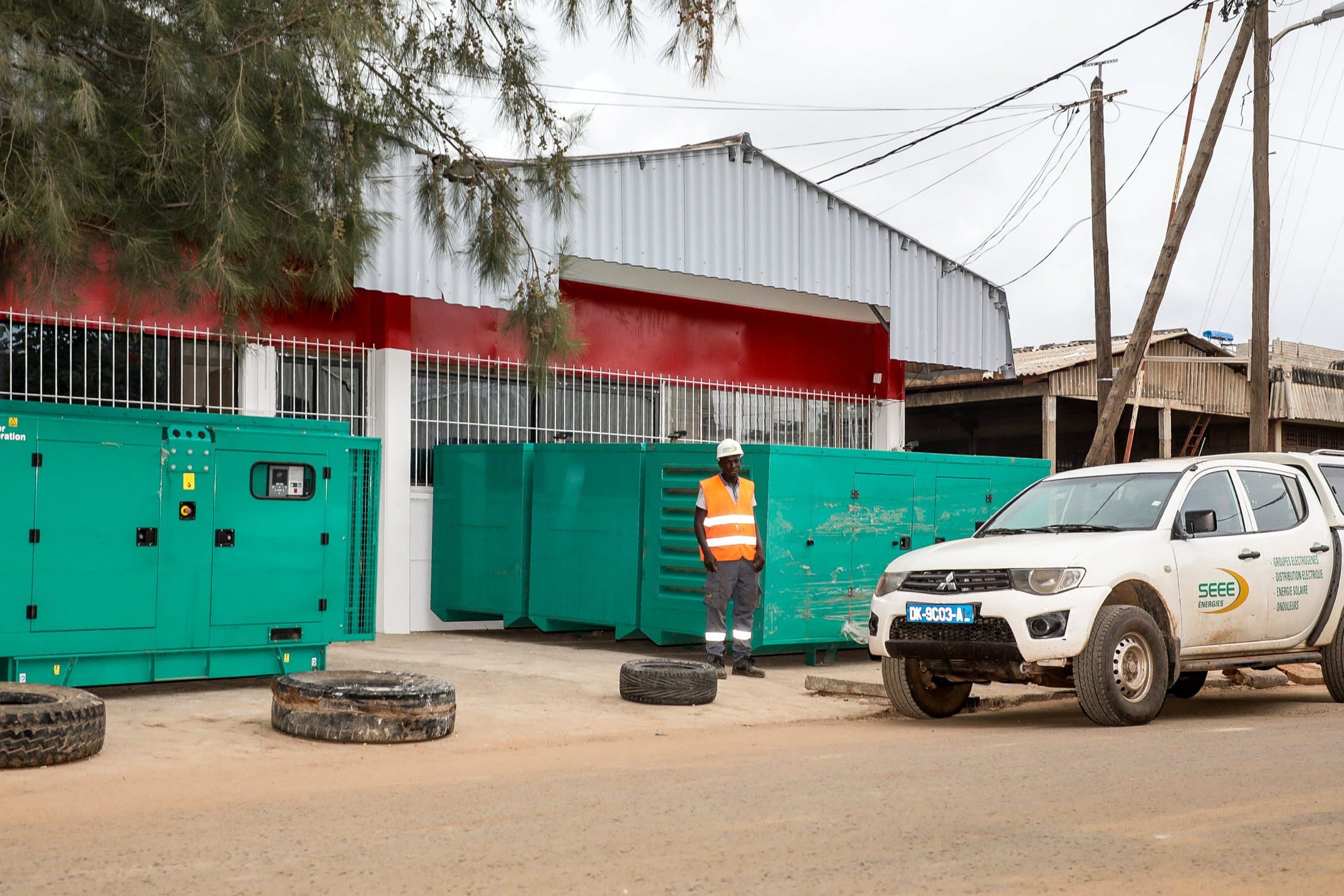 Groupes électrogènes Cummins devant l'atelier, un technicien en gilet orange et un pick-up SEEE Énergies